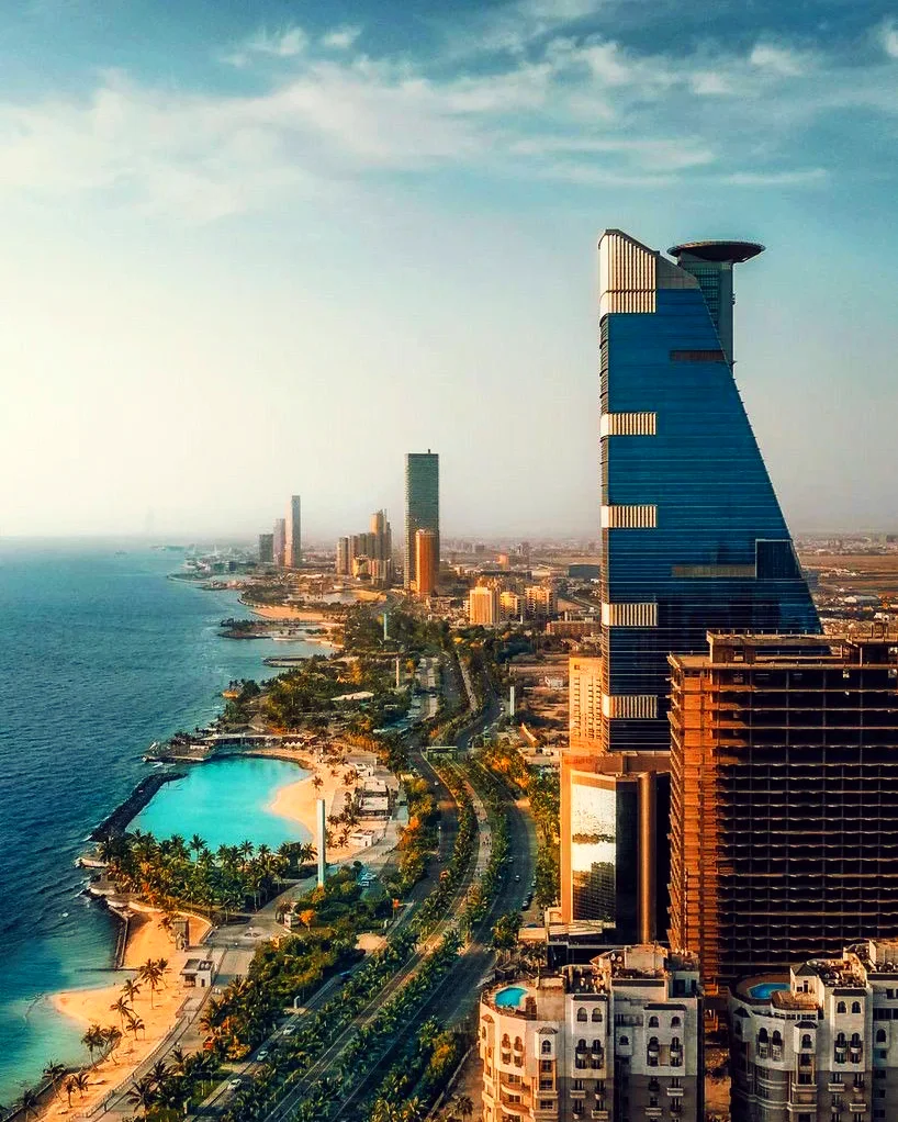 The coastline from the air, with a tall tower, a lagoon and a coastal road beside the sea.